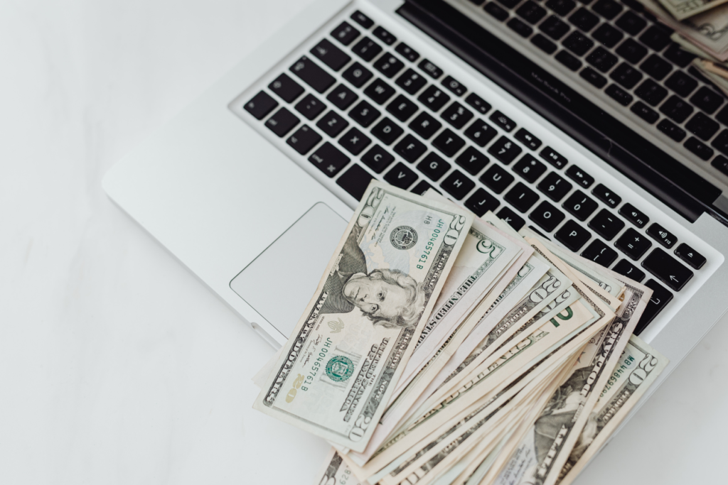 A pile of cash on a laptop keyboard symbolizing a focus on cost savings when hiring through an offshore staffing agency.